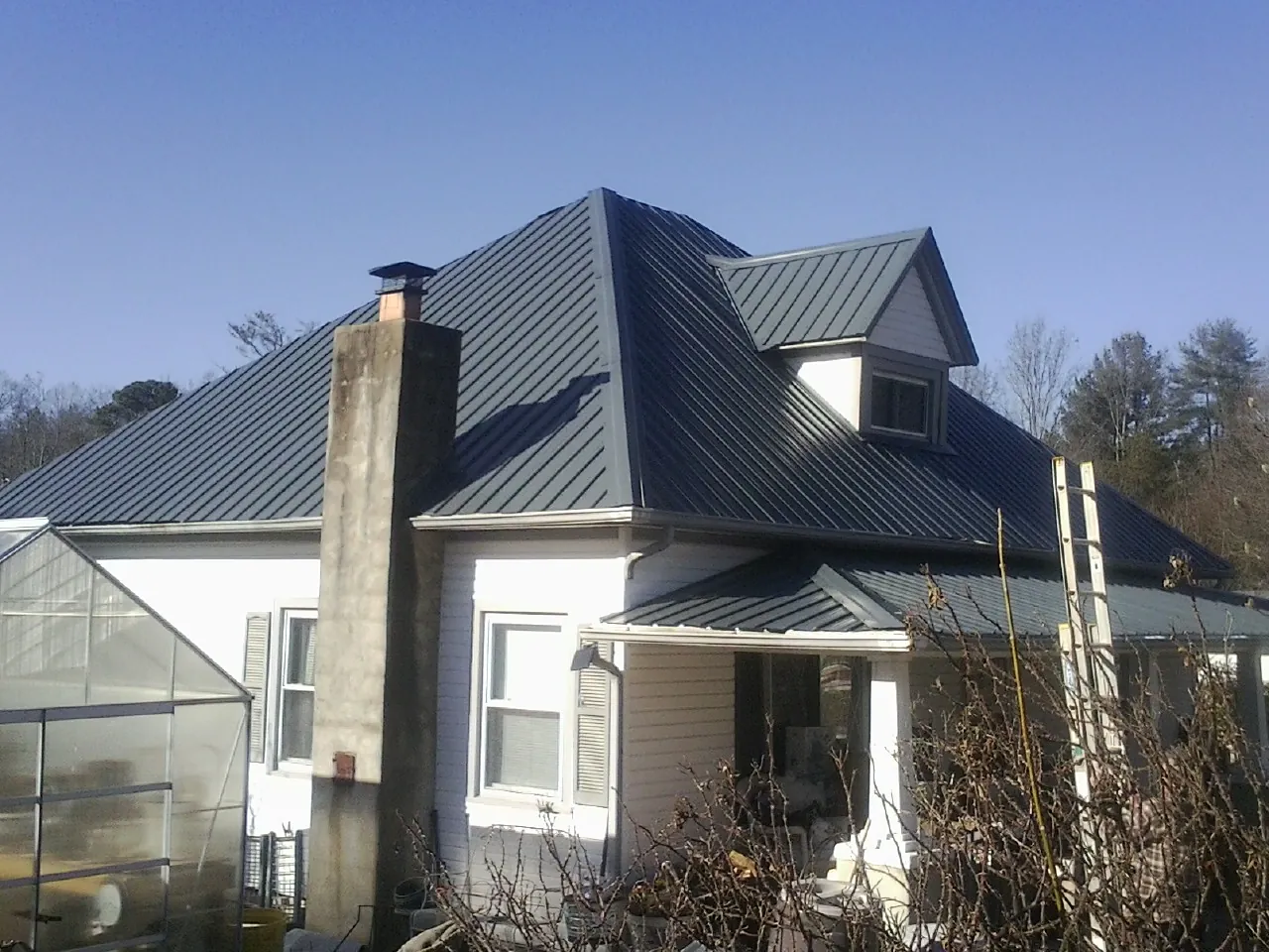 Dark blue standing seam metal roof on a white farmhouse with dormer — Slate & Tile Roof Repair by Roofing Brothers in Buffalo Mills