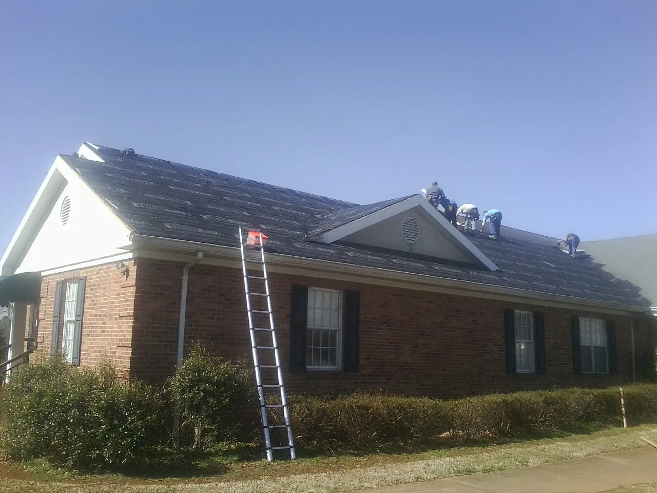 Crew tearing shingles off a brick ranch roof with a ladder set — Metal Roof Repair work by our crew in Buffalo Mills