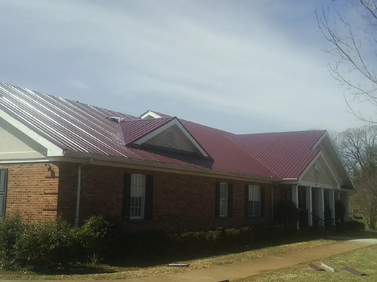 Red metal roof with gabled entries on a long brick building, from a Hail Damage Roof Repair job in Buffalo Mills