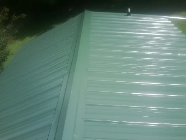 New green metal panels meeting at the ridge of a roof — Flat Roof Repair work by our crew in Buffalo Mills