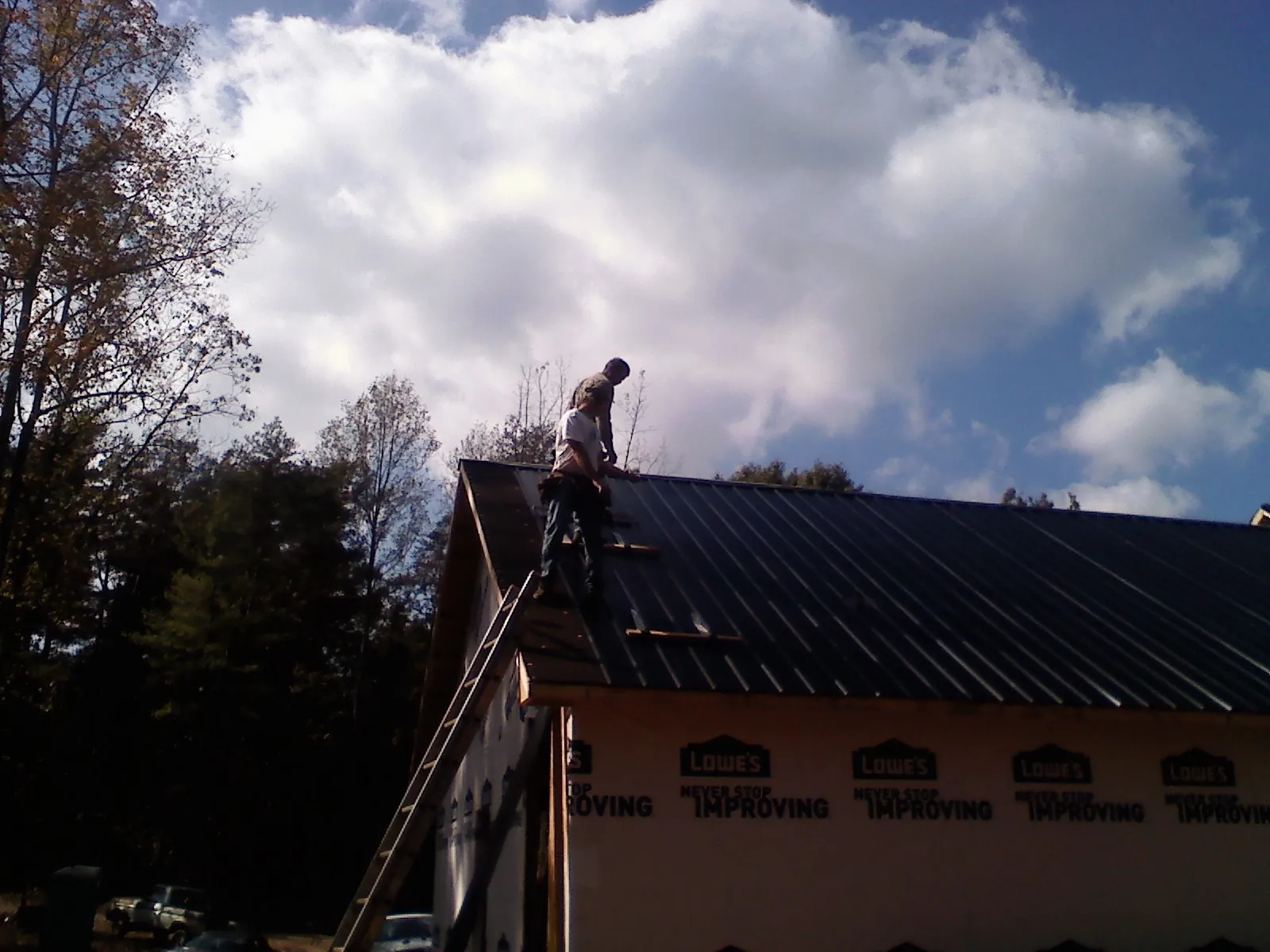 Roofer fastening dark metal panels high against a cloudy sky, from a Roof Inspection job in Buffalo Mills