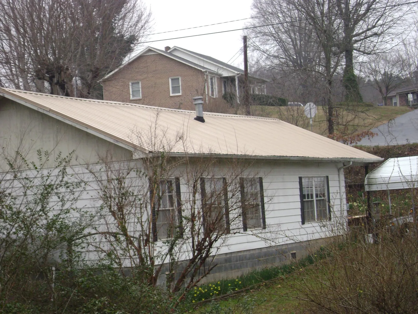 Tan metal roof on a white sided house set into a hillside — Commercial Roofing by Roofing Brothers in Buffalo Mills