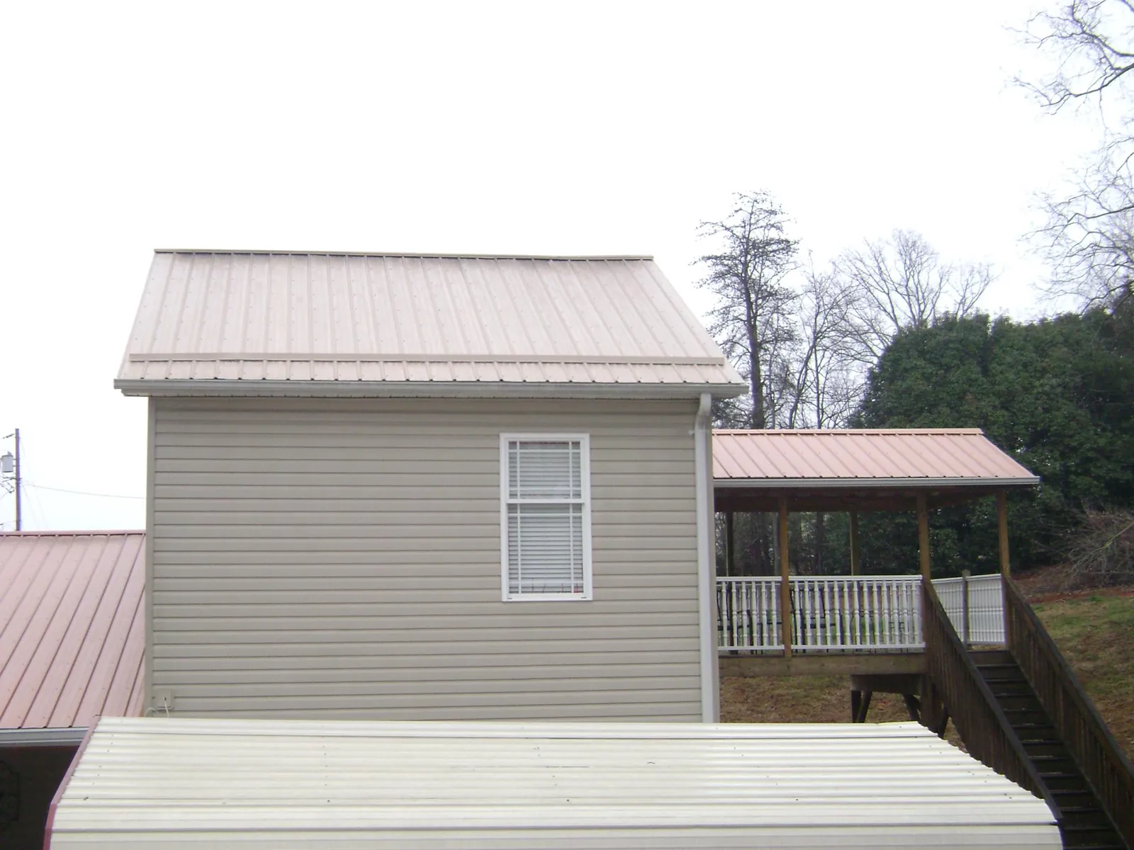 Tan metal roofs on a two story addition and attached porch, from a Roof Replacement job in Buffalo Mills